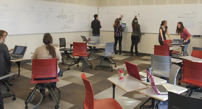 Students collaborating together during class lecture. Utilizing whiteboards and their computers to create a timeline.